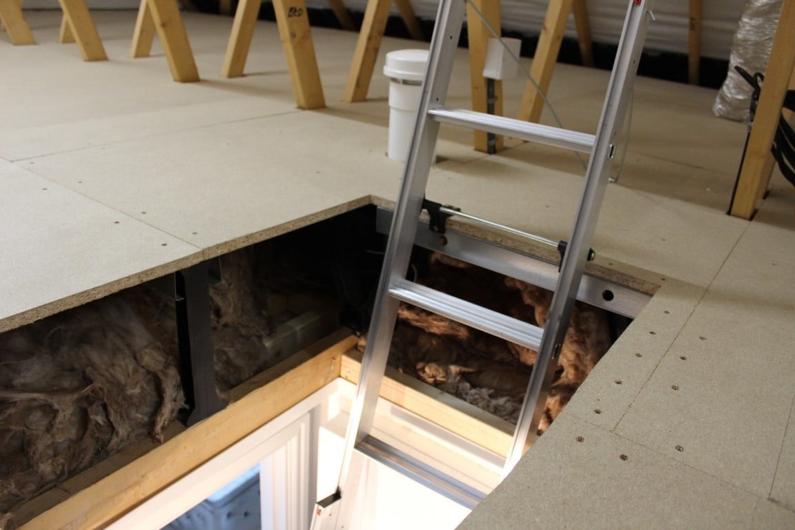 A draughty loft hatch that has had raised floor boards, insulation, and a metal access ladder installed.